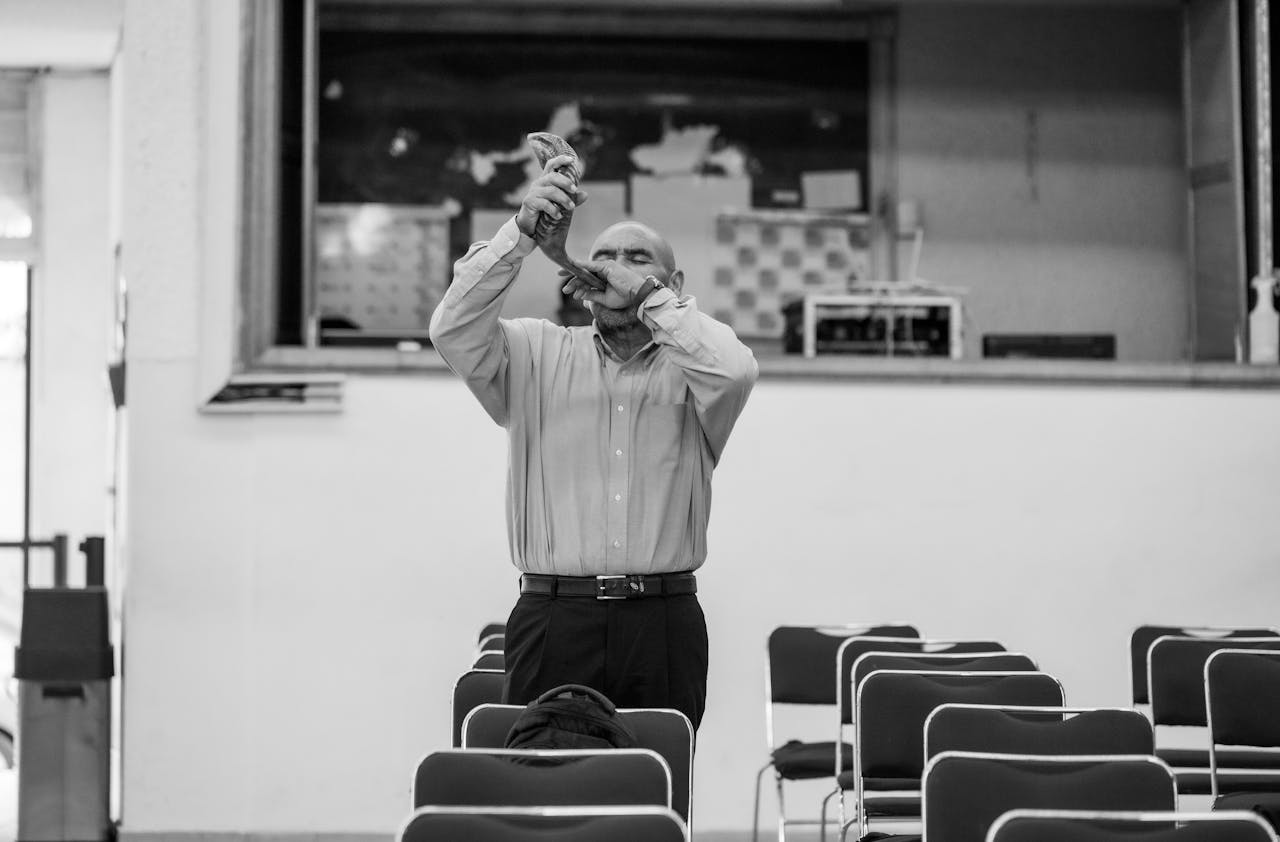 A bald man stands playing the shofar in an empty hall in Ciudad de México.