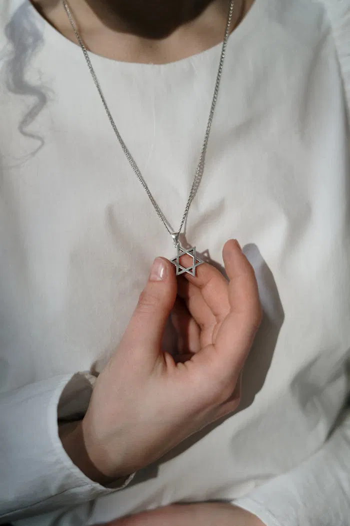 A detailed close-up of a woman holding a Star of David necklace, symbolizing Jewish faith.